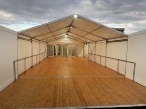 Spacious interior of a corporate event marquee with wooden flooring and steel-framed walls, set up by a hire company for corporate events.