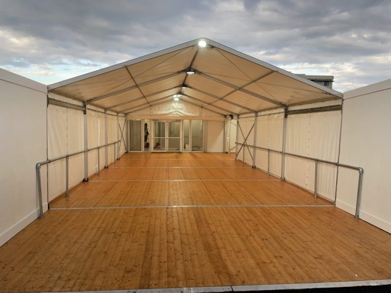Spacious interior of a corporate event marquee with wooden flooring and steel-framed walls, set up by a hire company for corporate events.
