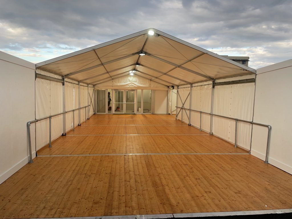 Spacious interior of a corporate event marquee with wooden flooring and steel-framed walls, set up by a hire company for corporate events.